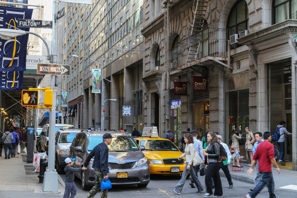 NEW YORK CITY, USA - MAY 19: A small street with shops in lower manhattan. Cars waiting at traffic lights - pedestrians walking across the street, May 19, 2014 in New York City.